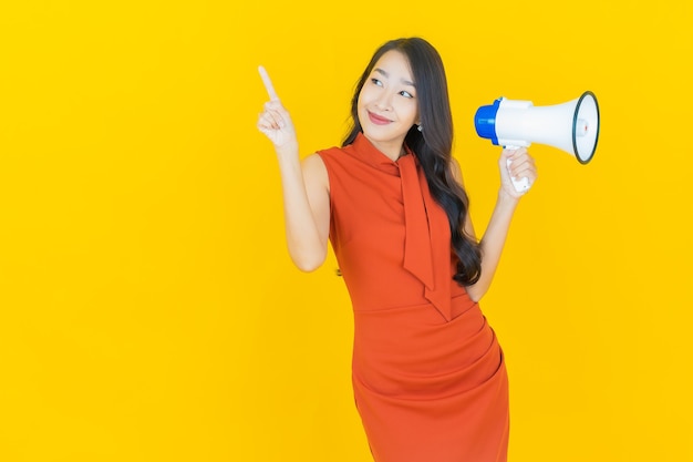 Portret mooie jonge Aziatische vrouw glimlach met megafoon op geel