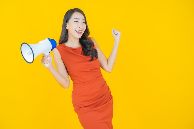 Portret mooie jonge Aziatische vrouw glimlach met megafoon op geel