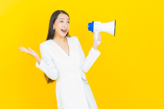 Portret mooie jonge aziatische vrouw glimlach met megafoon op gele kleur achtergrond on