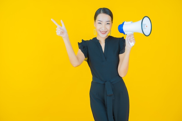 Portret mooie jonge Aziatische vrouw glimlach met megafoon op op geel