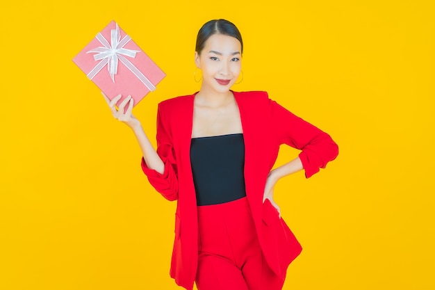 Portret mooie jonge Aziatische vrouw glimlach met rode geschenkdoos op geel