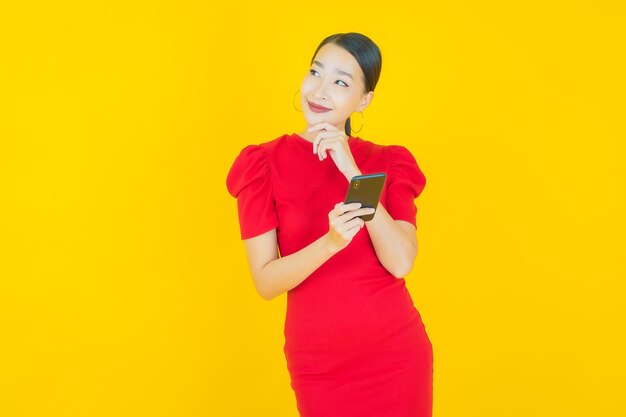 Portret mooie jonge Aziatische vrouw glimlach met slimme mobiele telefoon op geel