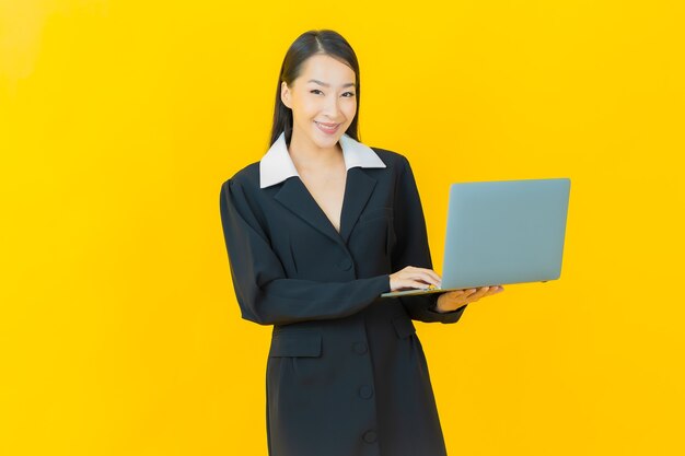 Portret mooie jonge Aziatische vrouw glimlacht met computer laptop op geïsoleerde muur