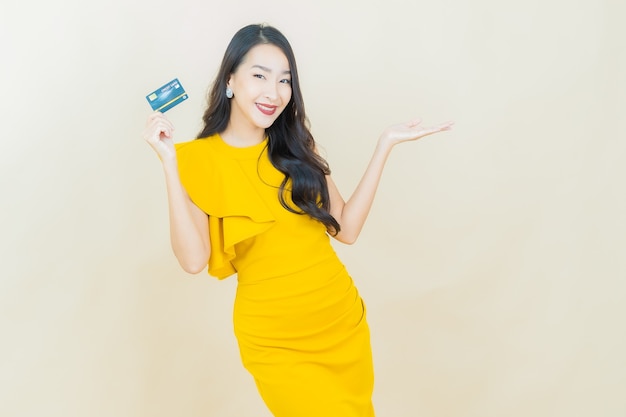 Portret mooie jonge aziatische vrouw glimlacht met creditcard op beige muur