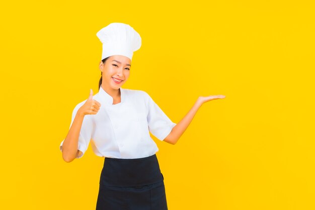 Portret mooie jonge Aziatische vrouw in chef-kok of kok uniform met hoed op gele geïsoleerde achtergrond