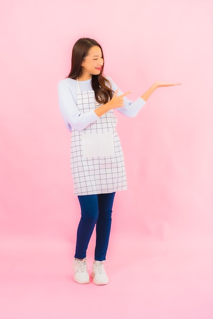 Portret mooie jonge aziatische vrouw in keukenslijtage met schort op roze geïsoleerde muur