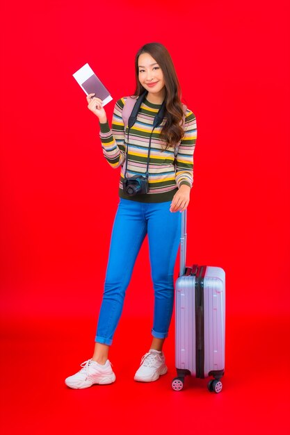 Portret mooie jonge Aziatische vrouw met bagage en instapkaart op rode muur