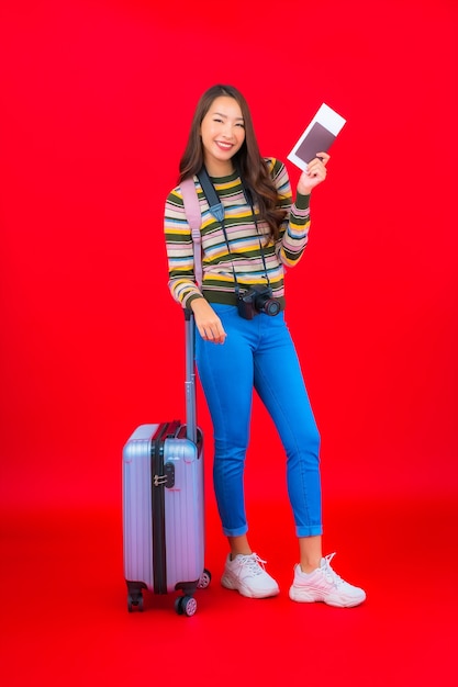 Portret mooie jonge Aziatische vrouw met bagage en instapkaart op rode muur