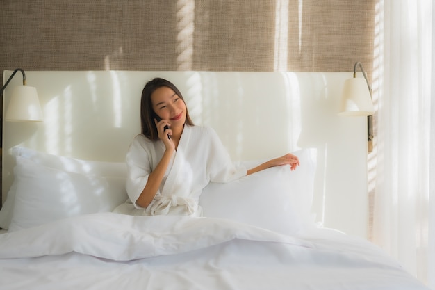Portret mooie jonge Aziatische vrouw met behulp van slimme mobiele telefoon op bed in de slaapkamer