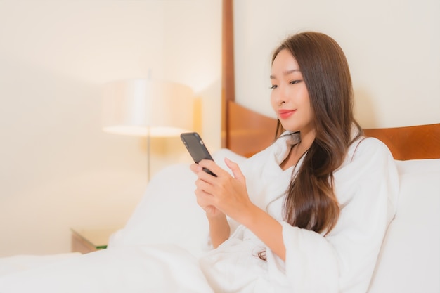 Portret mooie jonge Aziatische vrouw met behulp van slimme mobiele telefoon op bed in slaapkamer interieur