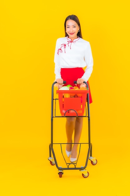 Portret mooie jonge aziatische vrouw met boodschappenmand van supermarkt op geel on