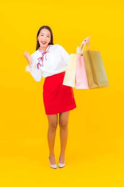 Portret mooie jonge aziatische vrouw met boodschappentas en creditcard op geel