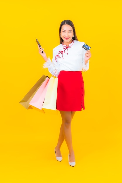 Portret mooie jonge aziatische vrouw met boodschappentas en creditcard op geel