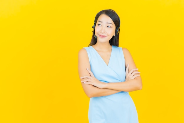 Portret mooie jonge aziatische vrouw met de servicecentrum van de call centre klantenzorg op gele kleurenmuur