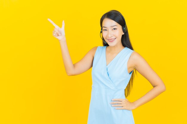 Portret mooie jonge aziatische vrouw met de servicecentrum van de call centre klantenzorg op gele kleurenmuur