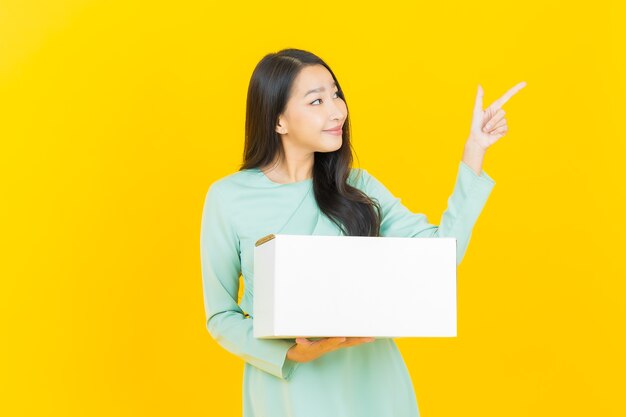 Portret mooie jonge aziatische vrouw met doos klaar voor verzending op geel