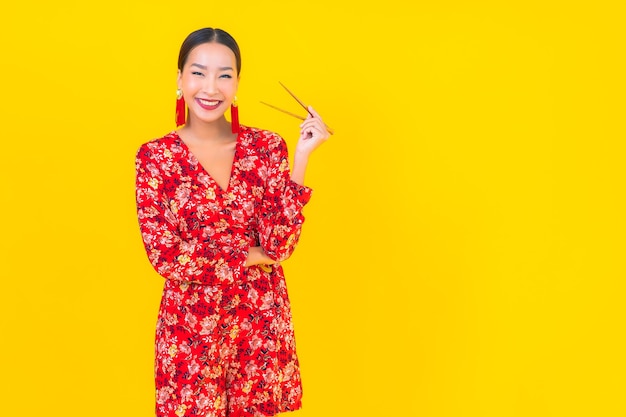 Portret mooie jonge Aziatische vrouw met eetstokjes op kleur geïsoleerde muur