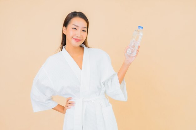 Portret mooie jonge Aziatische vrouw met flessenwater voor drank op beige