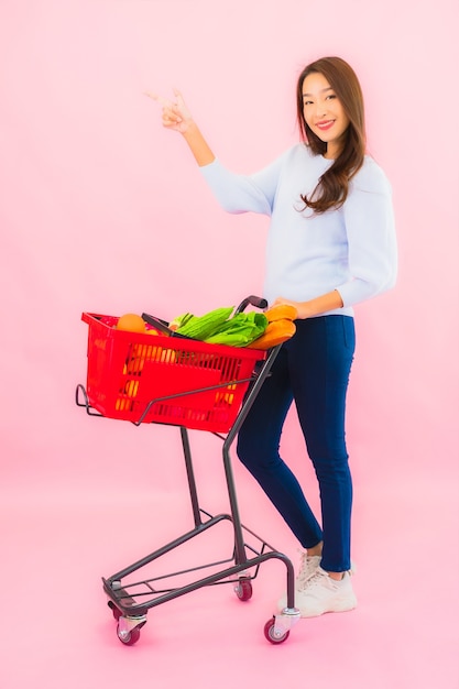 Portret mooie jonge aziatische vrouw met fruitgroente en kruidenierswinkel in mand op roze geïsoleerde muur