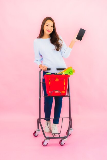 Portret mooie jonge Aziatische vrouw met fruitgroente en kruidenierswinkel in mand op roze geïsoleerde muur