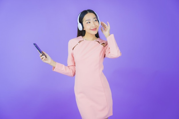 Portret mooie jonge aziatische vrouw met hoofdtelefoon en smartphone om muziek te luisteren op gele achtergrond