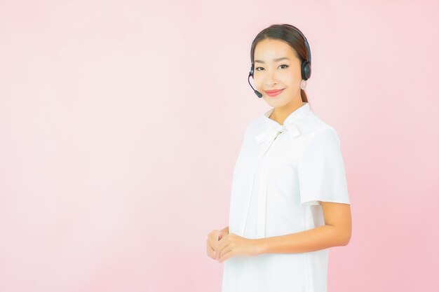 Portret mooie jonge Aziatische vrouw met hoofdtelefoon voor call centreerklant op roze muur