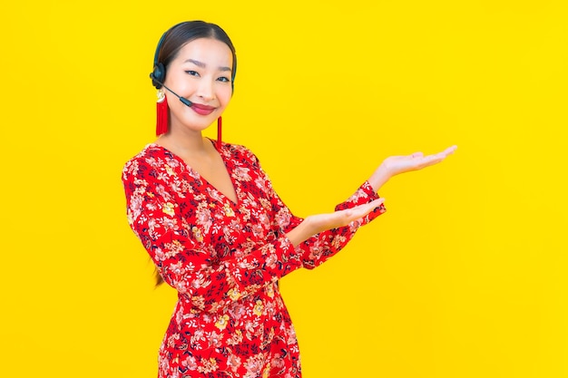 Portret mooie jonge aziatische vrouw met hoofdtelefoon voor de zorg van het klantencall centre op gele muur