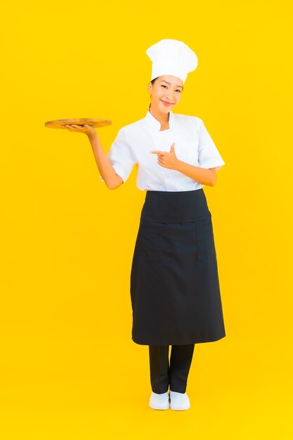 Portret mooie jonge Aziatische vrouw met houten snijplank op gele geïsoleerde achtergrond