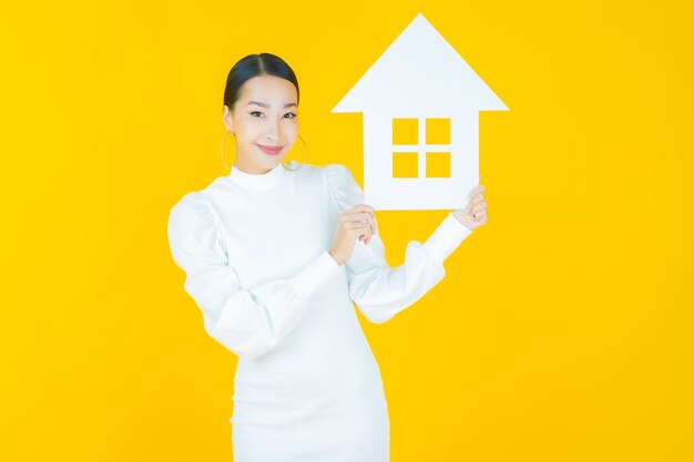 Portret mooie jonge aziatische vrouw met huis of huispapier teken op geel