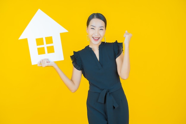 Portret mooie jonge aziatische vrouw met huis of huispapier teken op geel