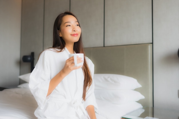 Portret mooie jonge Aziatische vrouw met koffiekopje in de slaapkamer