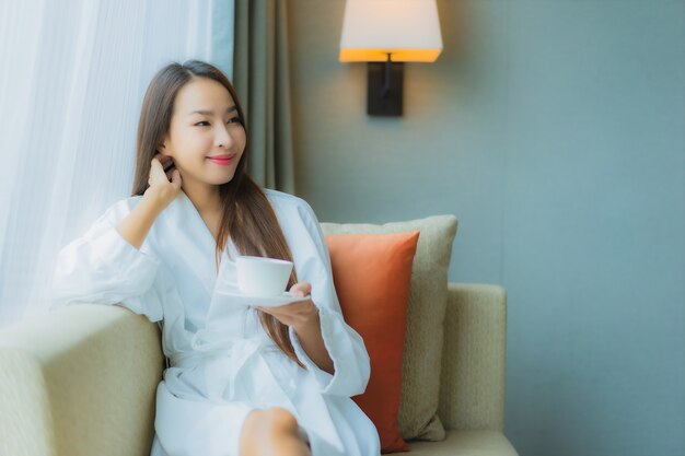 Portret mooie jonge Aziatische vrouw met koffiekopje op bank