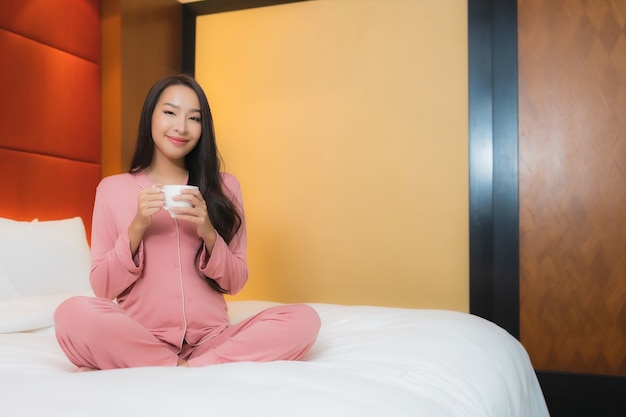 Portret mooie jonge Aziatische vrouw met koffiekopje op bed decoratie interieur van slaapkamer