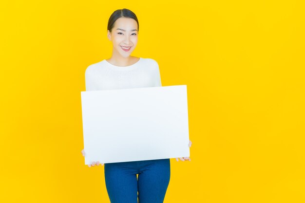 Portret mooie jonge Aziatische vrouw met leeg wit reclamebord op geel