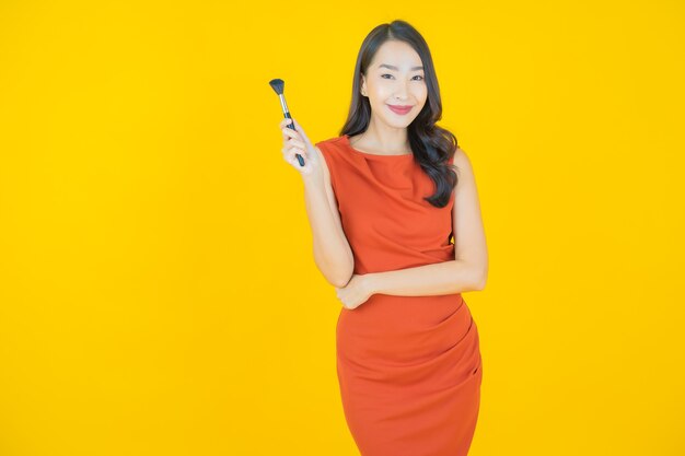 Portret mooie jonge Aziatische vrouw met make-up borstel cosmetica op geel
