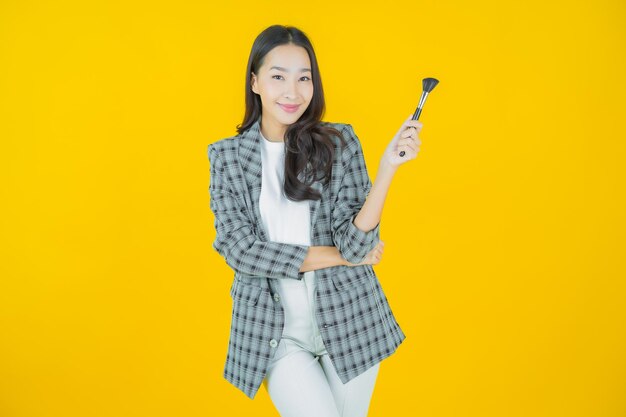 Portret mooie jonge Aziatische vrouw met make-up borstel cosmetische op kleur achtergrond