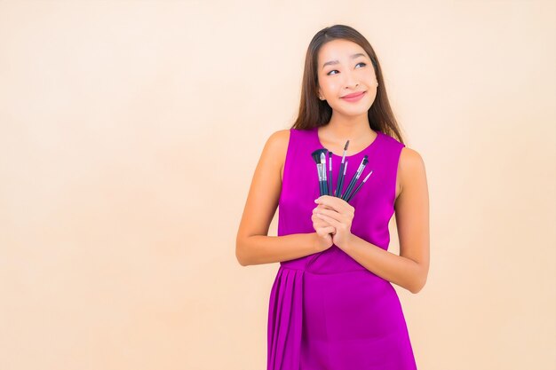 Portret mooie jonge Aziatische vrouw met make-up borstel op geïsoleerde kleur achtergrond