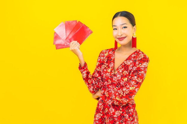 Portret mooie jonge Aziatische vrouw met rode enveloppen op gele muur