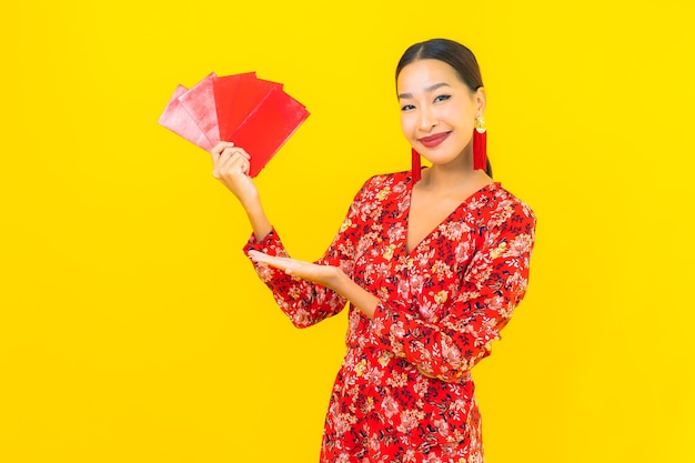 Portret mooie jonge Aziatische vrouw met rode enveloppen op gele muur