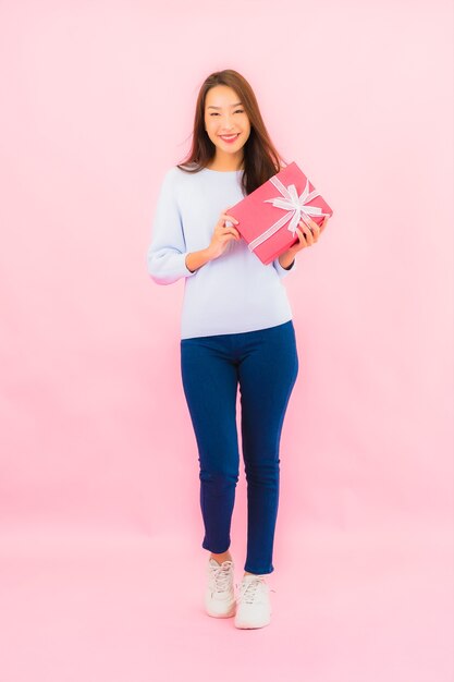 Portret mooie jonge aziatische vrouw met rode geschenkdoos op roze geïsoleerde muur