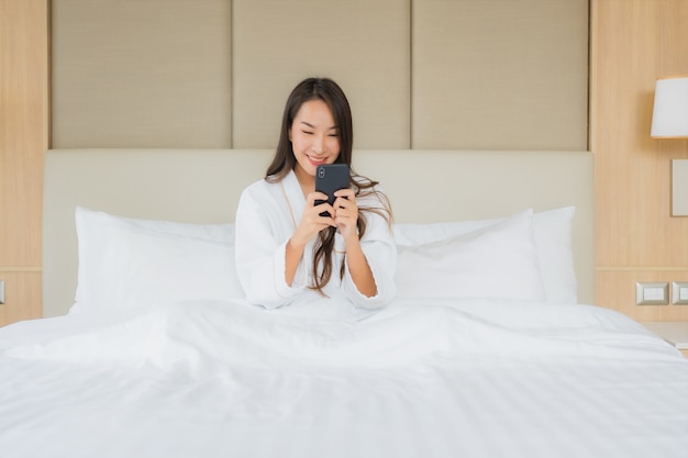 Portret mooie jonge Aziatische vrouw met slimme mobiele telefoon in de slaapkamer