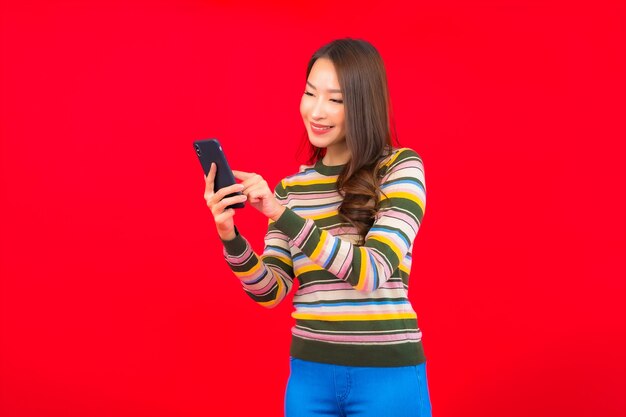 Portret mooie jonge Aziatische vrouw met slimme mobiele telefoon op rode muur