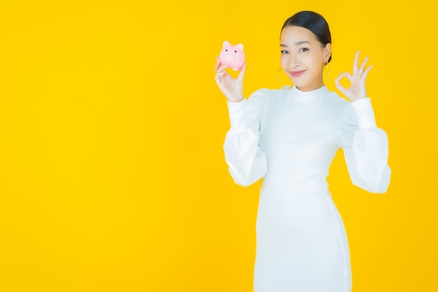 Portret mooie jonge Aziatische vrouw met spaarvarken op geel