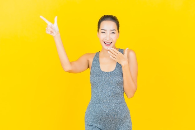 Portret mooie jonge aziatische vrouw met sportkleding klaar voor oefening op gele muur