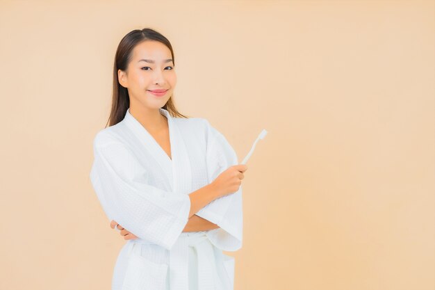 Portret mooie jonge Aziatische vrouw met tandenborstel op beige