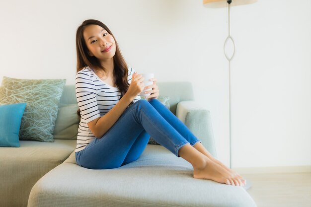 Portret mooie jonge Aziatische vrouw op bank met koffiekop