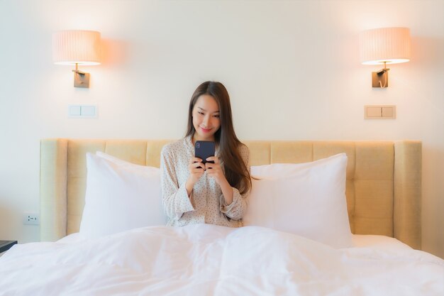 Portret mooie jonge Aziatische vrouw op bed met slimme mobiele telefoon