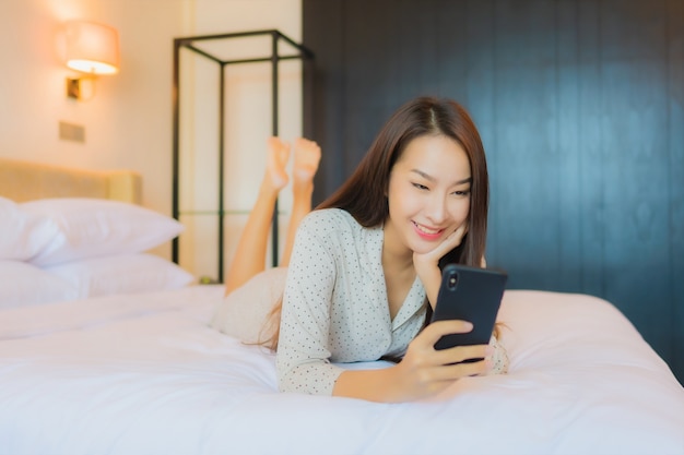 Portret mooie jonge Aziatische vrouw op bed met slimme mobiele telefoon