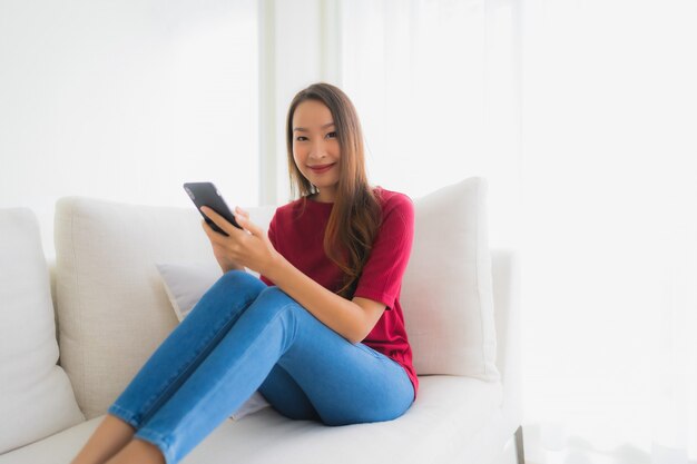 Portret mooie jonge Aziatische vrouwen die mobiele of slimme telefoon op bank met behulp van