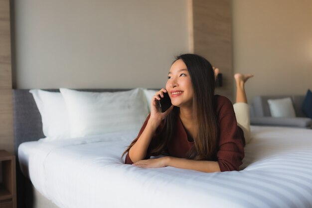 Portret mooie jonge Aziatische vrouwen die mobiele telefoon op bed met behulp van